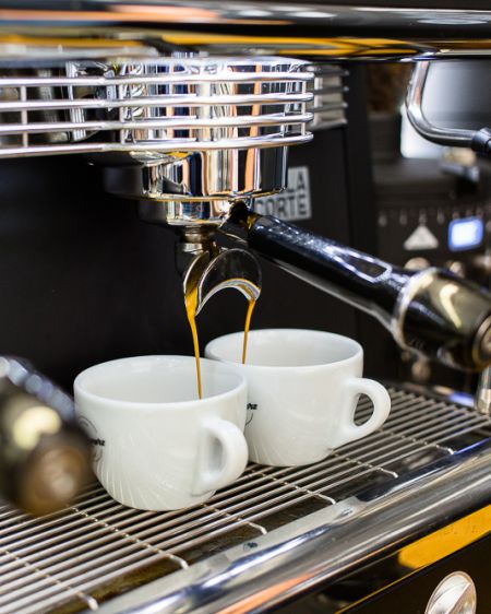 Two white coffee cups stand under a filter holder while coffee runs into the two cups