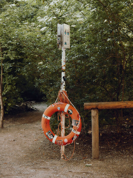 River surfing at the Eisbach in Munich Orange life belt hangs from a white sign with trees in the background