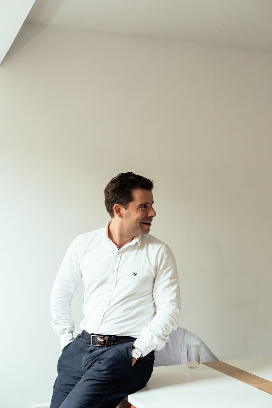 Interview mit Felix Haas: Das macht Gründer erfolgreich Felix Haas mit weißem Hemd und blauer Hose sitzt an der Tischkante und schaut zur Seite