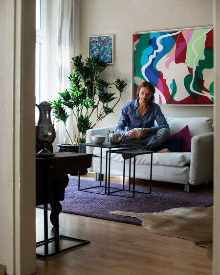 Markus Tenbusch is sitting on the sofa in his apartment with a coffee in a LAB cup from KPM Berlin.