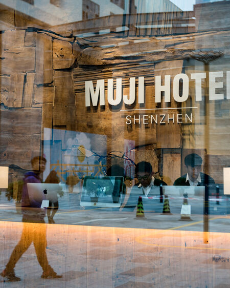 Reception of the Muji Hotel in Shenzen photographed through a window pane reflecting the street with passers-by
