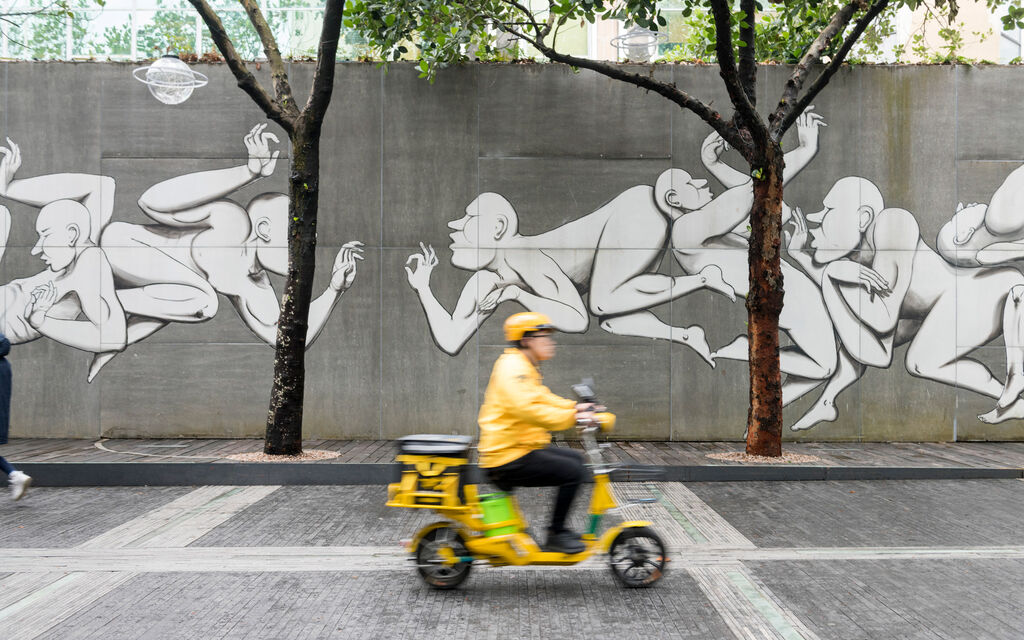 On the road with the Range Rover Sport Plug-in Hybrid: discovery tour of Shenzhen Yellow-clad scooter rider drives past a concrete wall sprayed with graffiti art in Shenzhen