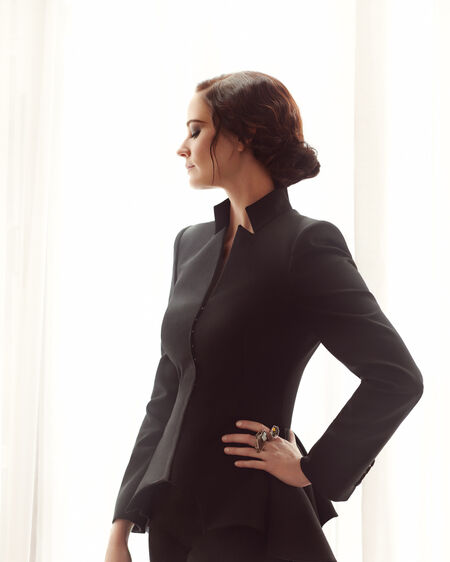 Eva Green in black pantsuit stands in front of windows with floor-length curtains