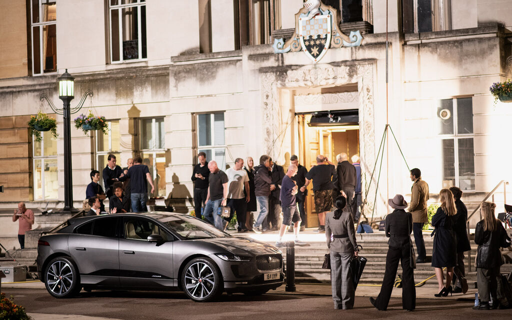Behind the scenes: Eva Green beim Werbedreh für den Jaguar I-PACE Grauer Jaguar I-PACE steht umgeben von mehreren Menschen vor Gebäude