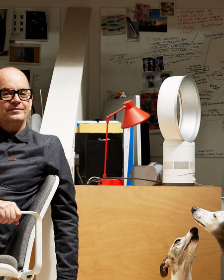 Brendan Walker sits on a chair in his office while two greyhounds lie on the floor next to him