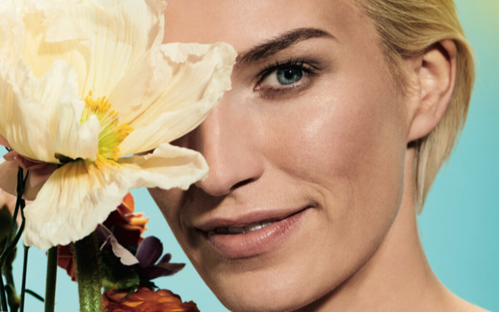 Close-up of a woman with natural make-up and several flowers in front of the right eye.