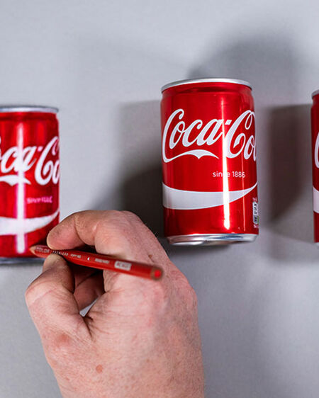 Howard Lee's hand draws a true-to-original cola can, next to which lie two real cola cans