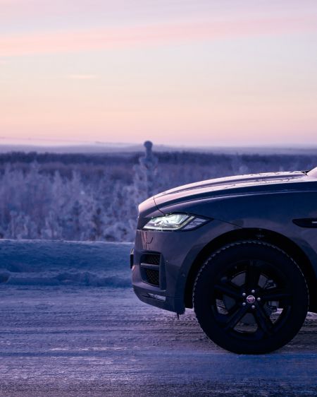 Jaguar F-PACE on a snowy road at sunset and purple sky