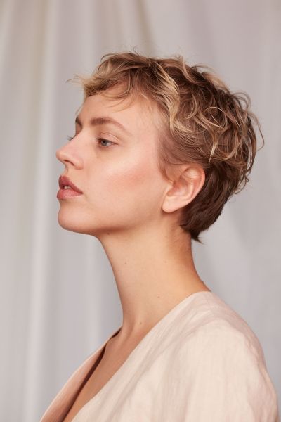 LUDWIG BECK Beauty: Covershooting für die Frühjahr-/Sommerausgabe 2020 Seitliche Aufnahme einer jungen Frau mit kurzen Haaren und natürlichen Makeup vor weißem Hintergrund