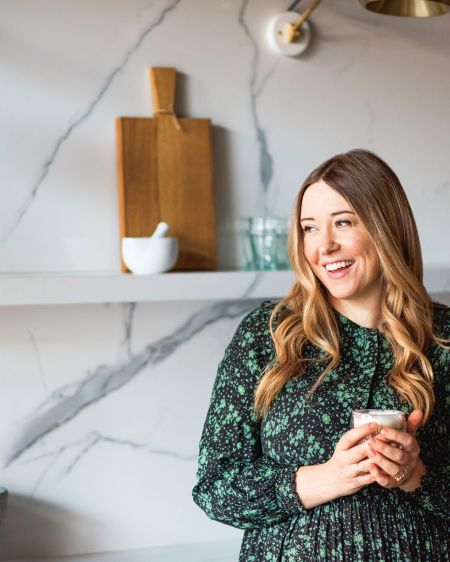 Star chef Anna Jones is leaning against her kitchen counter with a cup in her hand