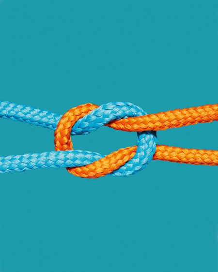 A turquoise and an orange rope are knotted together against a turquoise background
