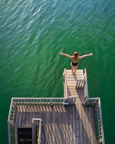 Iris Schmidbauer stands on a diving platform with outstretched arms above the Ammersee in Utting