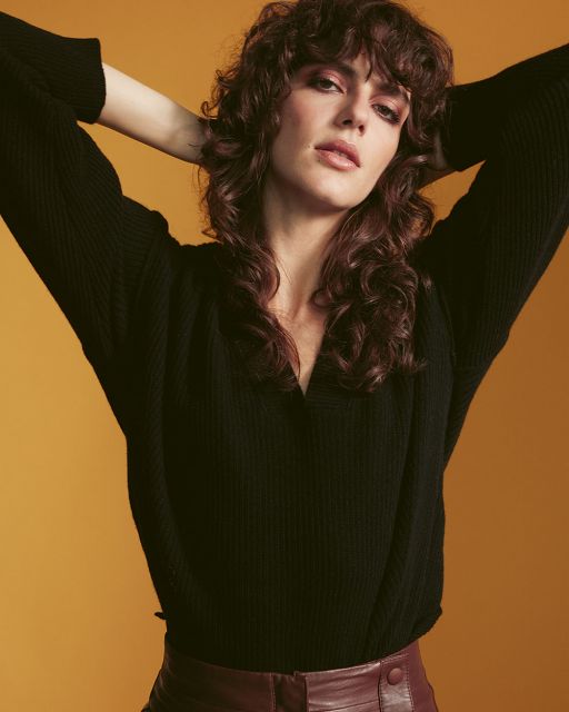 LUDWIG BECK Beauty: Cover shoot for the christmas 2020 issue Young woman with brown curls with her arms behind her head wears a black sweater and a wine-red leather skirt