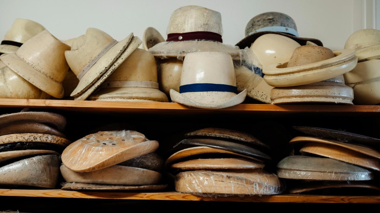 A shelf with multiple rows of finished and unfinished hats and hat forms of various sizes. A shelf with multiple rows of finished and unfinished hats and hat forms of various sizes.
