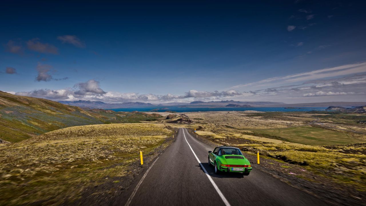 Ein grüner Porsche Oldtimer fährt über eine leere Landstraße durch eine bergige Landschaft in Island. Ein grüner Porsche Oldtimer fährt über eine leere Landstraße durch eine bergige Landschaft in Island.