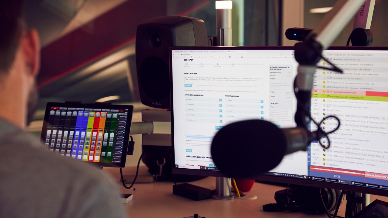 View over the shoulder of a man in a radio studio looking at multiple monitors displaying control interfaces and production timelines View over the shoulder of a man in a radio studio looking at multiple monitors displaying control interfaces and production timelines